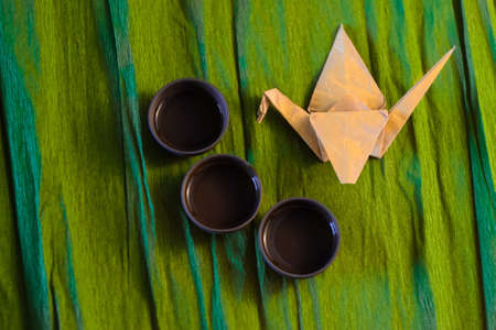 Three cups of ceramics and a origame  crane on the green background, close viewの写真素材