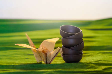 Three cups of ceramics and a origame  crane on the green background, close viewの写真素材