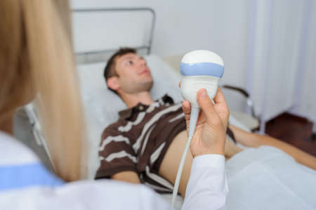 The lady  doctor  examination a man at abdomen with ultrasonography deviceの写真素材