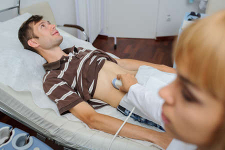 The lady  doctor  examination a man at abdomen with ultrasonography deviceの写真素材