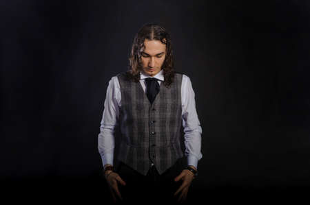 The handsome caucasian young man in a white shirt and suit standing, long hair, looking down black backgroundの写真素材
