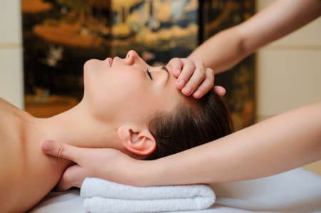 Spa procedure of neck massage. Close up view of beautiful young woman lying on back. Masseur /therapist massaging her faceの写真素材