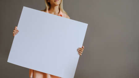 A pretty blonde girl with a whiteboard, close view, grey backgroundの写真素材