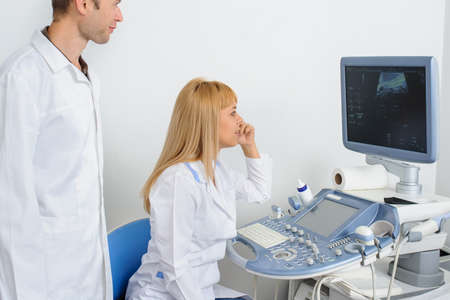 Two doctors looking at the ultrasonography divice in a medical officeの写真素材