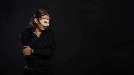 The handsome caucasian young man in a black shirt with white mask standing, black backgroundの写真素材