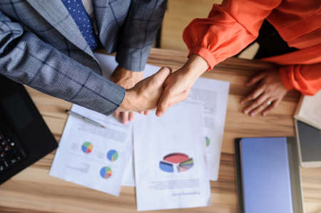 A business woman and man at a wooden office desk  handshaking, only hands, grey backgroundの写真素材