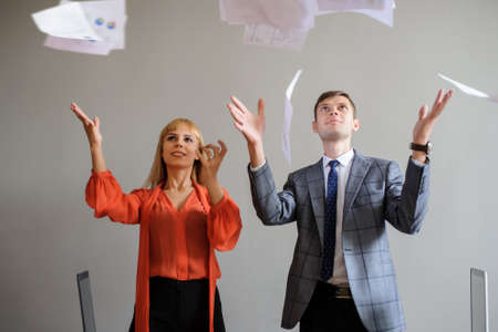 A business woman and man throwing papers up, at wooden office deskの写真素材