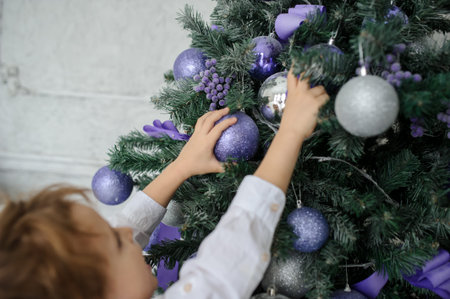 a 6-year blond boy decorating the christmas tree with purple toysの写真素材