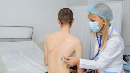 The doctor is consulting the patient with stethoscope at his back, back viewの写真素材