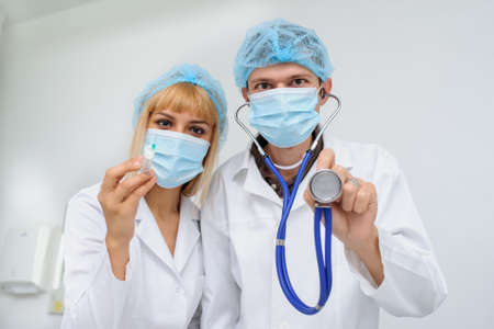 Two doctors with the masck, stethoscope in hand and injection, close viewの写真素材