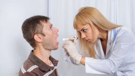 The doctor is looking in the mouth of the patient, close viewの写真素材