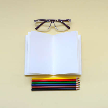 Some colored pencils with glases and opened notebook , top view, on a beige backgroundの写真素材
