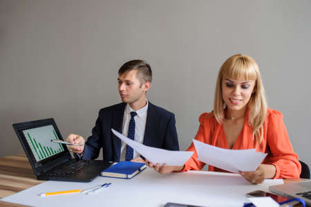 A business woman and man at a wooden office desk  looking at the project on the paper and computer with charts, grey backgroundの写真素材