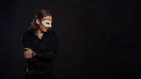 The handsome caucasian young man in a black shirt with white mask standing, black backgroundの写真素材