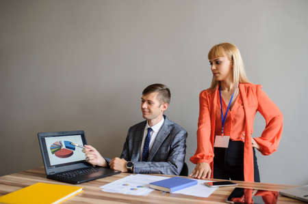 A business woman and man at a wooden office desk  working at the project on the paper and computer, grey backgroundの写真素材