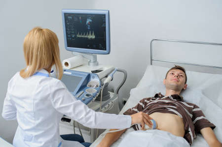 The lady  doctor  examination a man at abdomen with ultrasonography deviceの写真素材