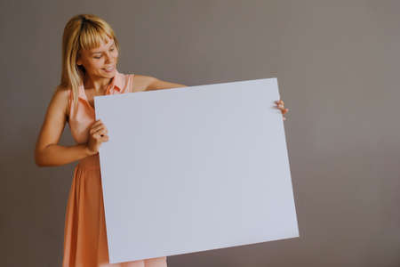 A pretty blonde girl with a whiteboard, close view, grey backgroundの写真素材