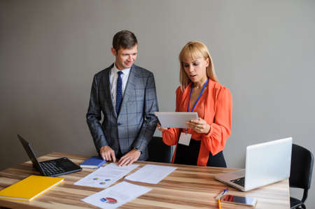 A business woman and man at a wooden office desk  working at the project on the paper and computer, grey backgroundの写真素材