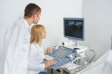 Two doctors looking at the ultrasonography divice in a medical officeの写真素材