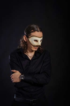 The handsome caucasian young man in a black shirt with white mask standing, black backgroundの写真素材