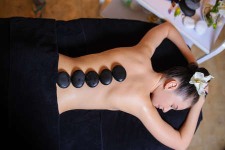 Stone therapy on a female client in beauty spa. Lateral view of a professional therapist masseuse doing hot stones massageon a female client.の写真素材