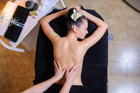 Women laying down on the massage bed in the spa with a flower in her hair.の写真素材