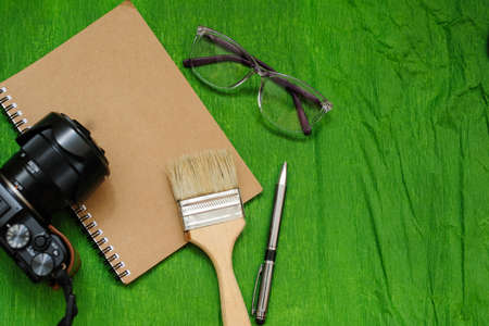 A notebook, a photo camera, glases, brush and pen, green backgroundの写真素材
