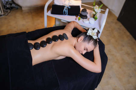 Stone therapy on a female client in beauty spa. Lateral view of a professional therapist masseuse doing hot stones massageon a female client.の写真素材