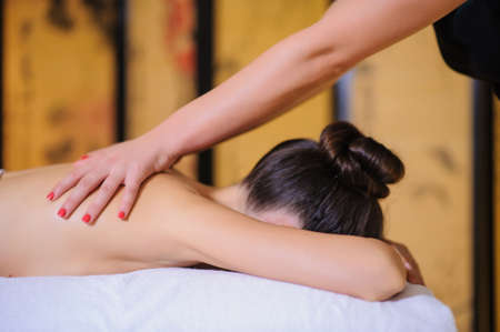 Masseur applying beauty massage on a female client Lateral view in the spa. Client laying down on the massage table in white towel.の写真素材