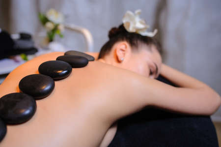 Stone therapy on a female client in beauty spa. Lateral view of a professional therapist masseuse doing hot stones massageon a female client.の写真素材