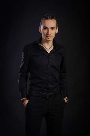 The handsome caucasian young man in a black shirt standing, black backgroundの写真素材