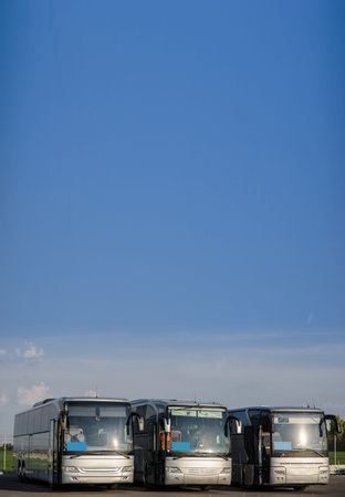 Three buses staying in the parking lot. Front view of the buses with blue sky and clouds.