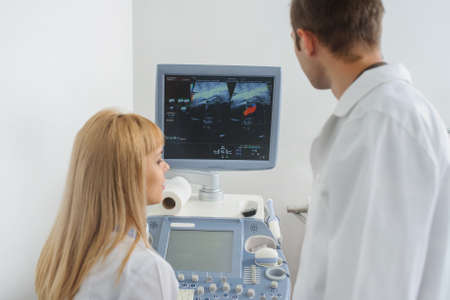 Two doctors looking at the ultrasonography divice in a medical officeの写真素材
