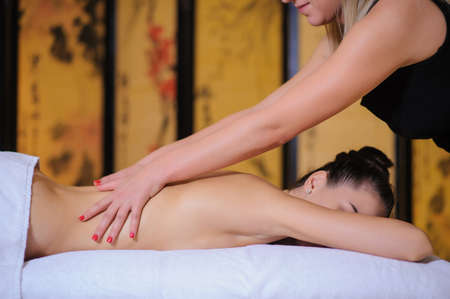Masseur applying beauty massage on a female client Lateral view in the spa. Client laying down on the massage table in white towel.の写真素材
