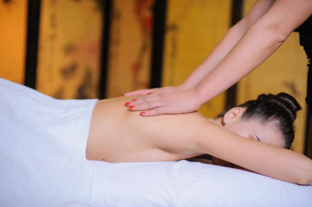 Masseur applying beauty massage on a female client Lateral view in the spa. Client laying down on the massage table in white towel.の写真素材