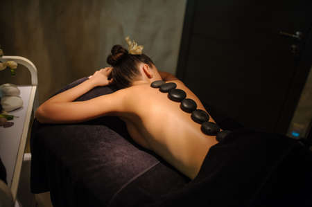 Stone therapy on a female client in beauty spa. Lateral view of a professional therapist masseuse doing hot stones massageon a female client.の写真素材