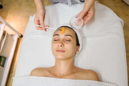 Close up head shot of Woman having curative facial massage. Therapist applying a mask with a brush on the face.の写真素材