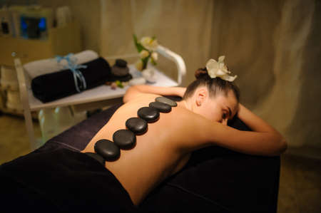 Stone therapy on a female client in beauty spa. Lateral view of a professional therapist masseuse doing hot stones massageon a female client.の写真素材