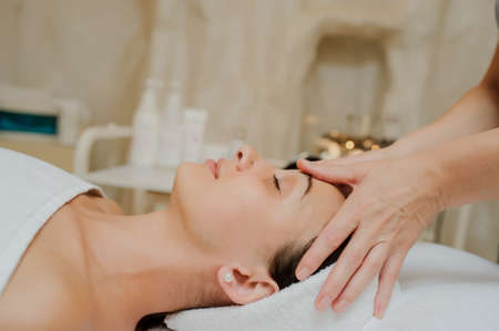 Lateral view  of a Woman having curative facial massage. Therapist applying pressure with fingers on forehead. Massage with handsの写真素材