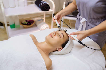 Lateral view of woman facial massage spa procedure. Electric stimulation facial skin care. Microcurrent lift face. Beauty spa procedure. Anti aging rejuvenation non surgical treatment in medical interior roomの写真素材