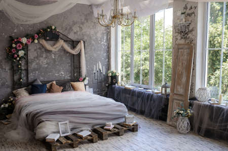 A wood bed in a photo studio decorated with flowers and curtains and sorrounded by books, frames, candle sticksの写真素材