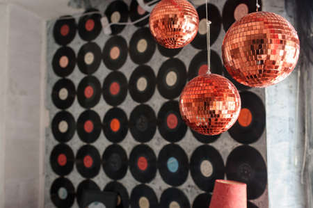 A wall full of ordered vinyl records with diffrent colors in the middle near a window decoreted with hanged red shiny spheres and a red lampの写真素材