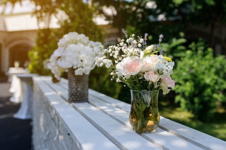 Closeup photo of a white bench from wood timbers with a bouquets of flowers in vases on it on a...