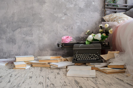Closeup photo of a vintage typewriter covered with white and pink flowers on a wooden floor with...