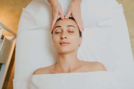 Top view of Woman having curative facial massage. Therapist applying pressure with fingers on forehead. Massage with handsの写真素材