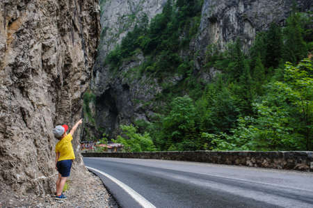 The back of a 6-years blond boy  near a rocky mountain and a roadの写真素材