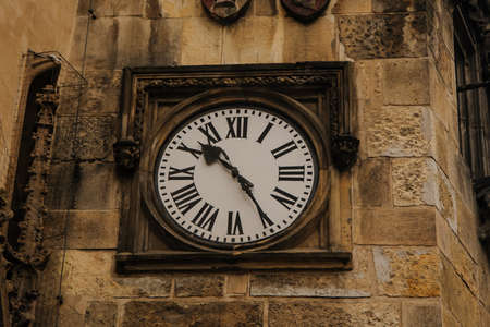 Closeup photo of a medieval clock on the wall of a very old brown historical buildingの写真素材