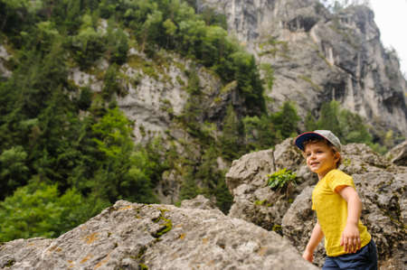 Lateral view of a 6-years blond boy near a rocky mountain surrounded by grassの写真素材