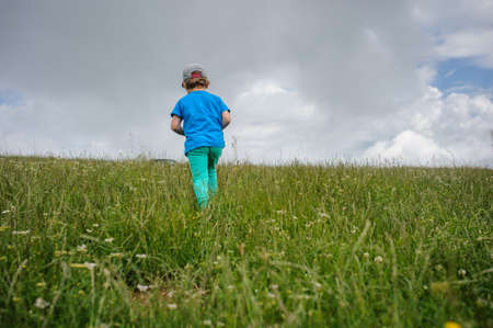 The back of a 6-years blond boy running on the top of the mountainの写真素材