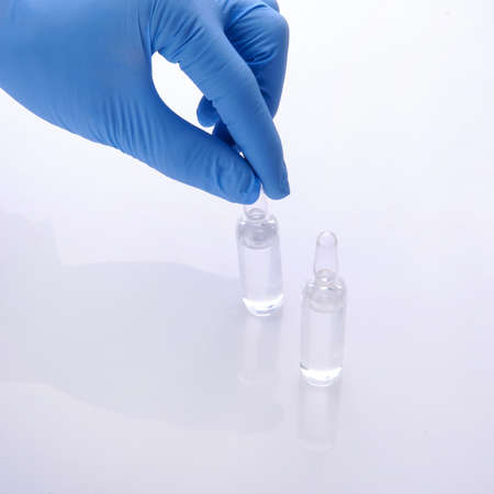 a hand of a doctor in a blue glove holding the superior part of one ampoule from two on a white backgroundの写真素材